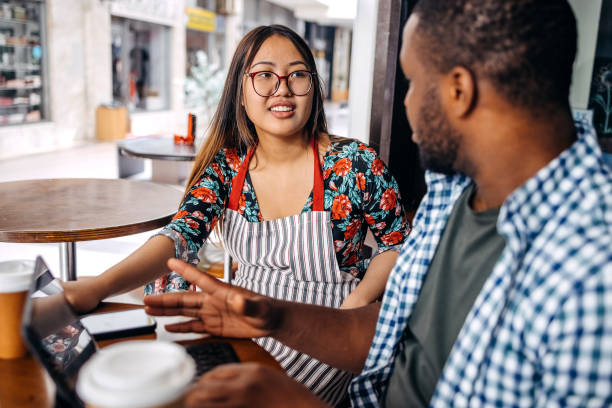 istock Asian waitress working at cafe serving regular customer and sitting next to him having casual talk 2174878606