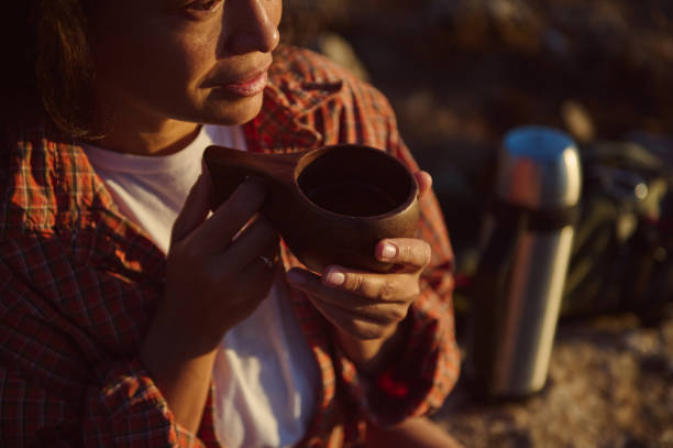 istock Woman enjoying a warm beverage outdoors while sitting on a rock with a thermos by her side during sunset in nature 2174884670