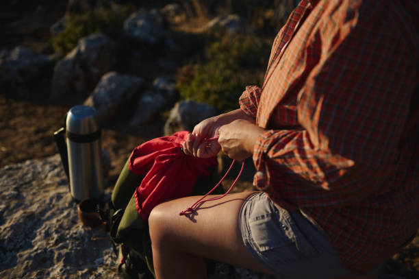 A hiker tightens a drawstring on their backpack amidst rocky terrain, with warm sunset lighting enhancing the outdoor experience.