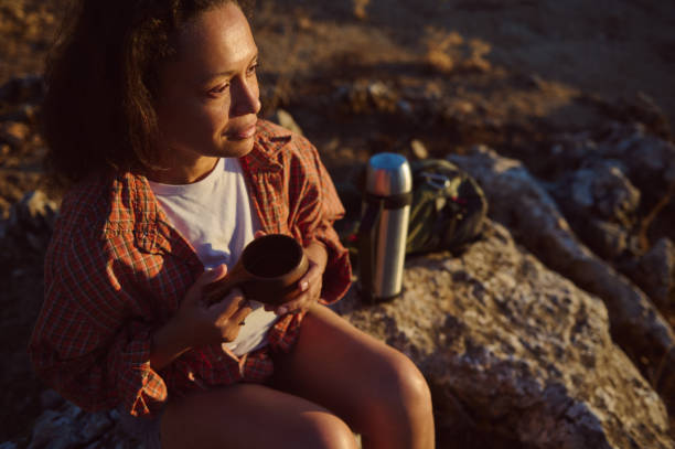 istock Woman enjoying a warm drink while sitting on a rocky surface during a peaceful sunset hike in nature 2174884796