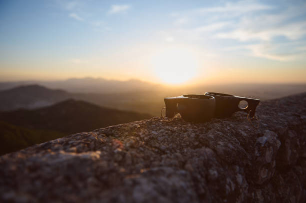 istock Sunset view with two cups on rock wall, silhouetted against scenic mountain landscape. 2174884805
