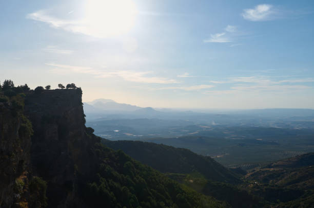 Panoramic landscape from a steep mountain cliff, showcasing lush valleys and distant hills under a brilliant blue sky, capturing the serene beauty of nature.