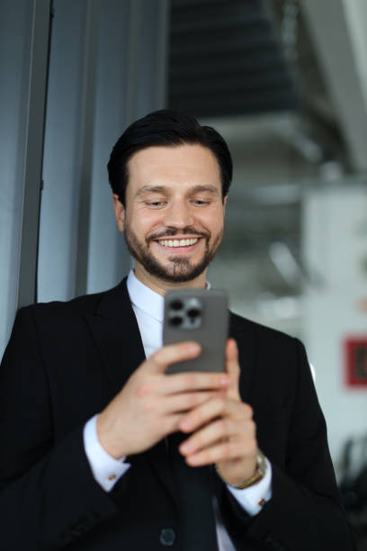istock A man in a suit is smiling while looking at his cell phone. He is wearing a tie and he is in a professional setting 2174887536