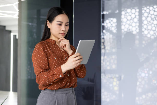 istock Focused Asian woman using tablet in modern office setting, showcasing technology and professional work environment with attention to detail. 2174898415