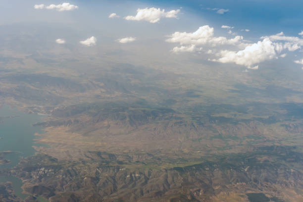 View of the ground from the window of a passenger airliner. Clouds and populated areas in the folds of the terrain.