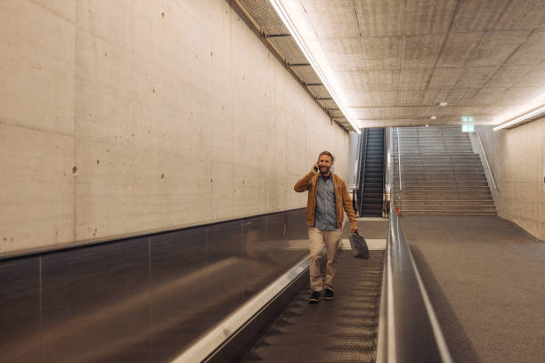 istock Businessman in train station taking a moving walkway while on the phone 2174903572