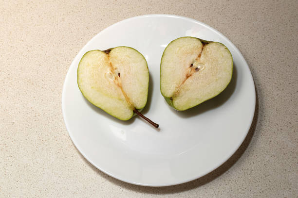 A juicy green pear cut in half on a white plate on the kitchen table, close-up, top view