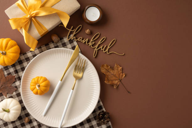 istock A Thanksgiving table setting featuring pumpkins, a gift with a yellow ribbon, and a thankful decoration on a brown background 2174905654