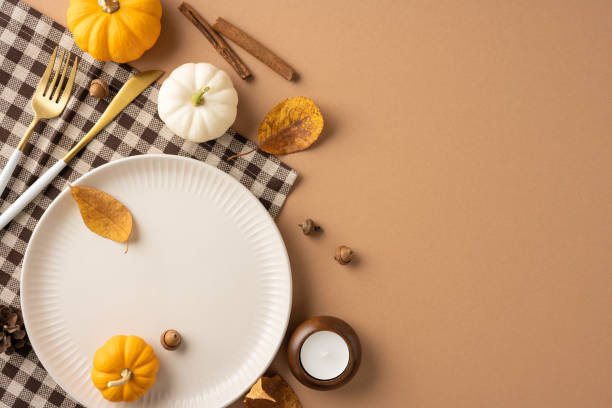 istock Flat lay of a Thanksgiving table setting featuring a plate, small pumpkins, and autumn leaves on a brown background. The scene captures fall's warm, inviting atmosphere 2174905655