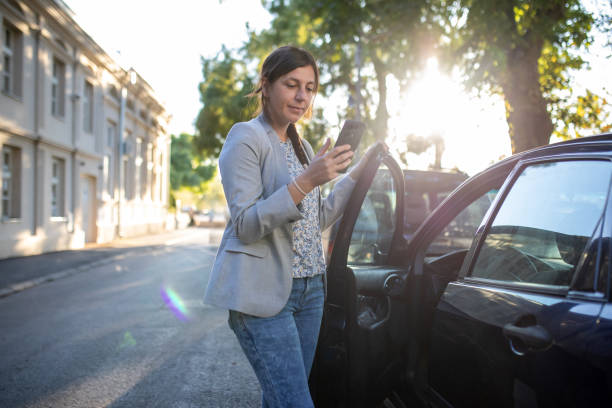 istock Young woman using her mobile phone while getting into the car. 2174917365