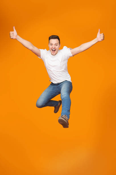 istock Funny man jumping with raised arms over orange background 2174923877