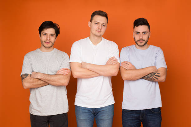 Three men posing confidently against a vibrant orange backdrop, showcasing casual attire and relaxed body language in a modern setting