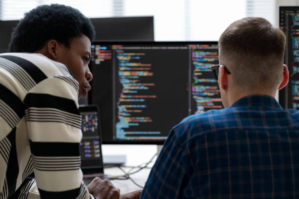 A team of software developers engages in real-time collaboration to compile source code and address bugs in a modern software development office. Dressed in business wear and casual clothing, work at desks with laptops and computer monitors, discussing solutions and refining code. a team of software developers engages in real-time collaboration to compile source code and address bugs in a modern software development office. dressed in business wear and casual clothing, work at desks with laptops and computer monitors.
