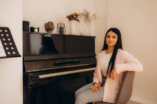 istock Music teacher turning on smartphone for online lesson, while sitting at table with synthesizer at home. Woman learns music, playing piano online at home interior. Female play piano synthesizer 2174940324