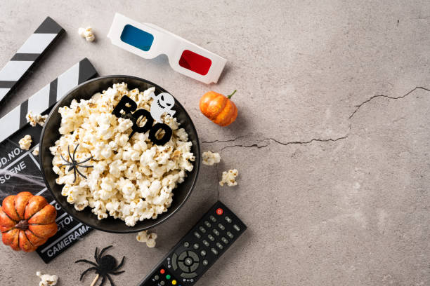 Halloween themed setup for a movie night featuring popcorn, remote control, 3D glasses, clapboard, and pumpkin decorations