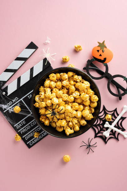 istock Bowl of popcorn with Halloween vertical themed decorations including a clapperboard, toy spiders, pumpkin glasses, and skeleton bones 2174946247