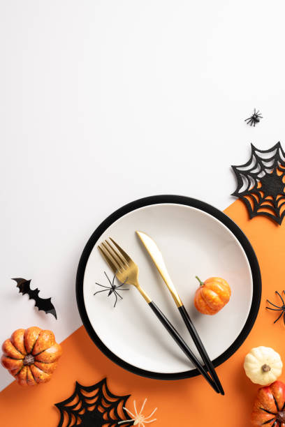 istock Elegant Halloween vertical themed table setting with pumpkins, spiders, and bats on an orange and white background 2174946268