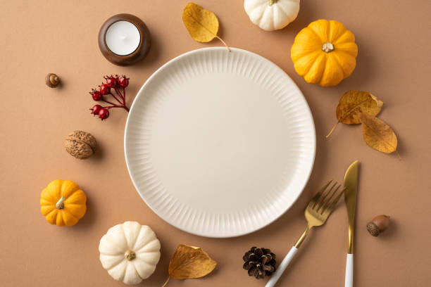 istock Flat lay of a Thanksgiving-themed table setting featuring mini pumpkins, autumn leaves, and a white plate on a brown background 2174946310