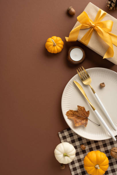 istock Elegant vertical Thanksgiving table arrangement featuring small pumpkins, a wrapped gift, and a stylish plate setting on a brown background 2174946320