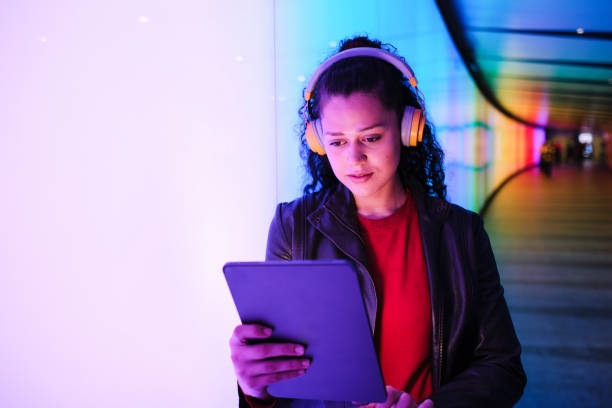 istock Young woman using digital tablet with headphones in neon corridor 2174950211