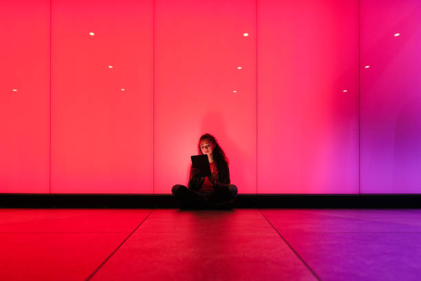istock Young woman using digital tablet sitting on floor by glowing wall 2174950493