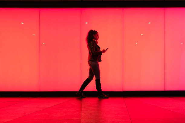 istock Young woman walking by red lit wall using smartphone 2174952157
