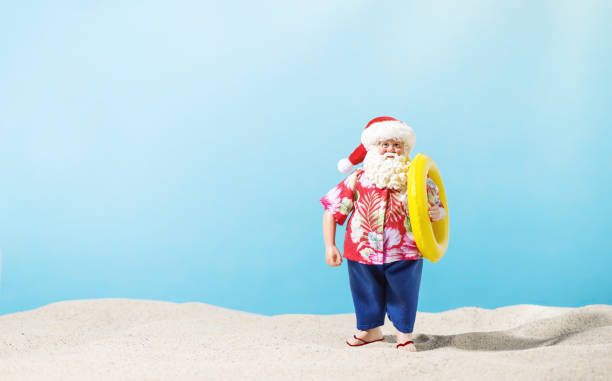 Santa Claus with inflatable ring on sand over blue background. Christmas vacation, tropical climate.