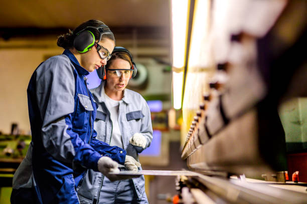 Skilled Female Workers Operating Press Brake in Industrial Setting Two focused Caucasian women in safety gear use a press brake machine, working diligently in a well-lit manufacturing facility. manufacturing occupation stock pictures, royalty-free photos & images