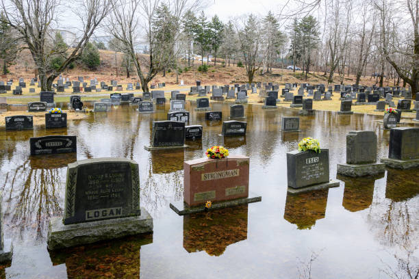 Saint John, NB, Canada - March 30, 2024: A flooded cemetery. Water surrounds many of the grave markers. Overcast sky.
