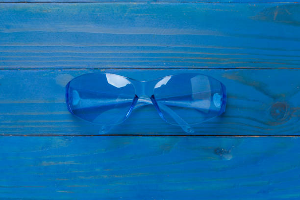 Safety glasses on wooden background, top view