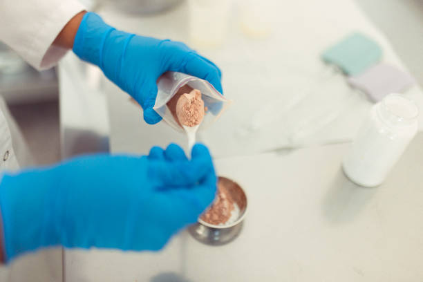 An unrecognizable woman with protective gloves makes a mixture for natural sulfate-free soap