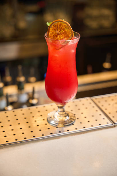 Close-up of a bright red cocktail with a dried orange slice garnish placed on a bar counter
