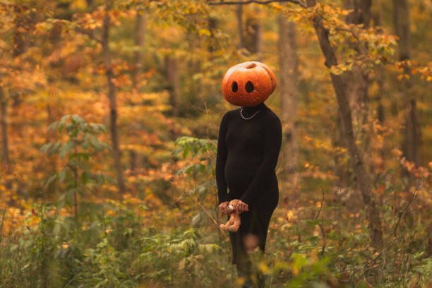 Pregnant Woman with Pumpkin Head holding Toy in Hand in Autumn Forest Halloween Holidays