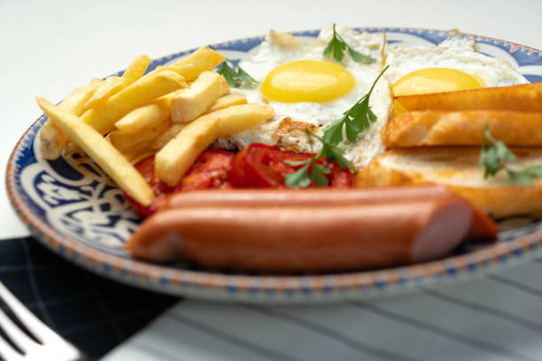 Breakfast plate with fried eggs, sausage, tomatoes, and fries served on a decorative blue plate close up