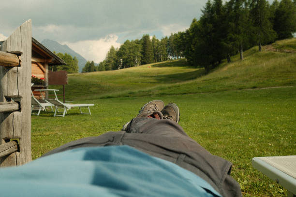 Hiker is lying in a meadow, enjoying the view of a mountain chalet in the distance