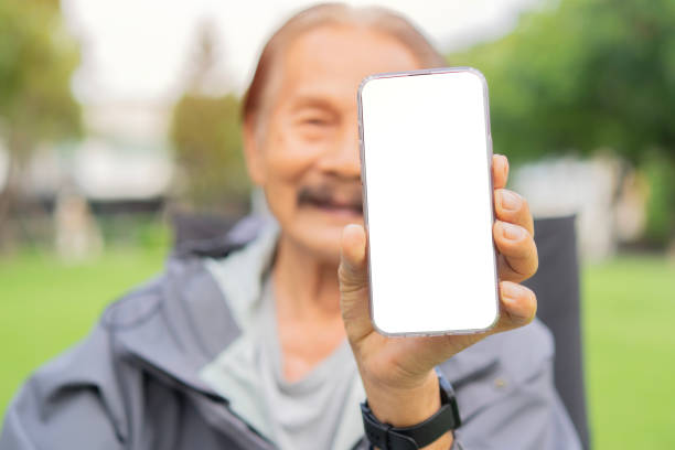 istock Senior man with a beard smiling while standing outside in sunlight, showing mobile phone with blank screen. 2175083644
