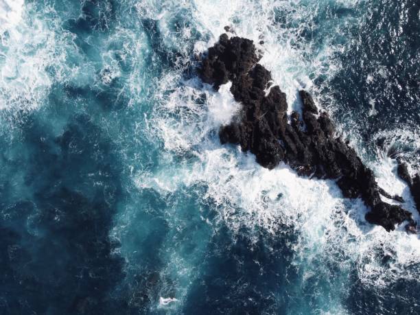 This captivating aerial view captures the mesmerizing patterns created by ocean waves as they crash and swirl across the surface. The rich blues and turquoises of the water contrast beautifully with the white froth of the breaking waves, creating an intricate tapestry of movement and color. The image reveals the dynamic energy of the ocean, showcasing the rhythmic ebb and flow that defines coastal landscapes. This perspective offers a unique appreciation for the natural artistry of the sea, evoking a sense of tranquility and wonder.