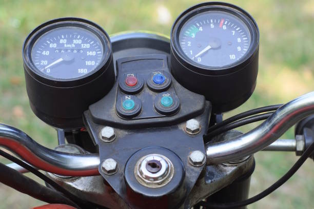 two black round plastic speedometers on the dashboard of an old motorcycle on a summer street