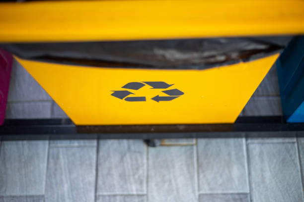 A trash can with a recycle sign on it. The trash can is on a gray tile floor