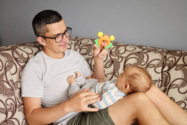 istock Father interacting with his little infant boy while playing games and communicating affectionately expressing joy of childhood in their cozy home while sitting on couch in living room 2175117304