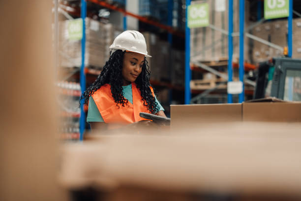 istock African american woman logging inventory in warehouse with boxes, hard-working. 2175118513