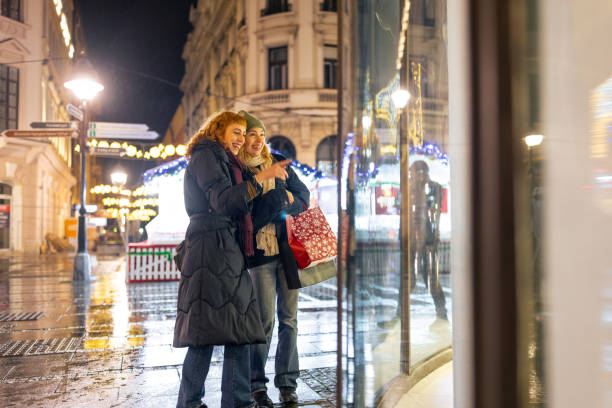 Two women enjoying an evening out, window shopping in a beautifully lit urban area, reflecting the joy and ambiance of city nightlife.