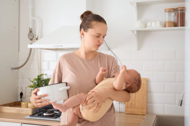 istock Exhausted mommy multitasking in the kitchen holding her baby son doing her morning routine cooking and carrying her newborn despite exhaustion from the demands of motherhood 2175140878