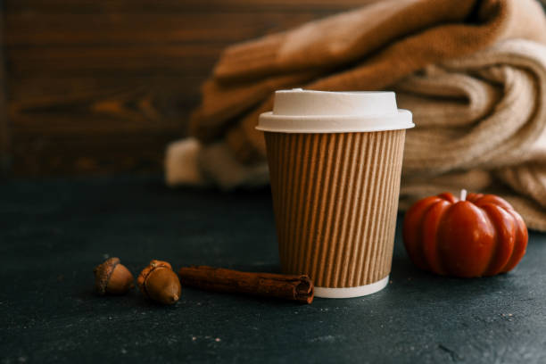 istock Paper coffee cup with acorns and cinnamon stick on a dark surface with cozy sweaters in the background. Perfect for autumn, cozy, or warm drink concepts 2175143444