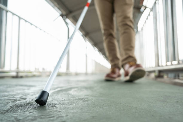 Young blind man walking in city with walking stick. Visually impaired man difficult to traveling on the road wearing sun glasses Cross the road cross the footbridge