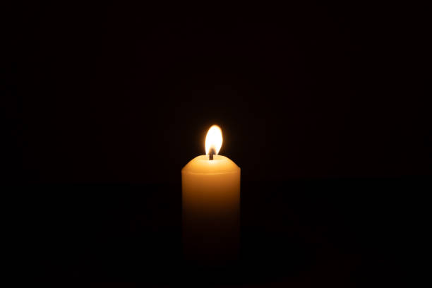 istock A single burning candle flame or light glowing on a big white candle isolated on red or dark background on table in church for Christmas, funeral or memorial service 2175151471