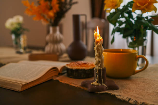 Cozy dining table with a warm autumnal atmosphere featuring a yellow cup, an open book, a muffin, and decorative vases with yellow flowers. The scene evokes a sense of relaxation and comfort.