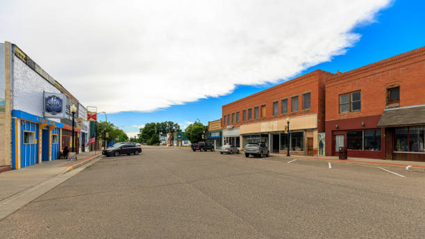 Exploring small town center of Las Animas, Colorado. Historic brick buildings adorn quiet main street with parking lots Las Animas, Colorado, Bent County, USA - May 31, 2024: Quiet main street in Las Animas, Colorado. Wide street lined with historic brick buildings housing local businesses. Parked cars indicate some activity. Partly cloudy sky with patches of blue. Streetlamps and American flag enhance classic small-town American atmosphere. colorado flag art pictures stock pictures, royalty-free photos & images