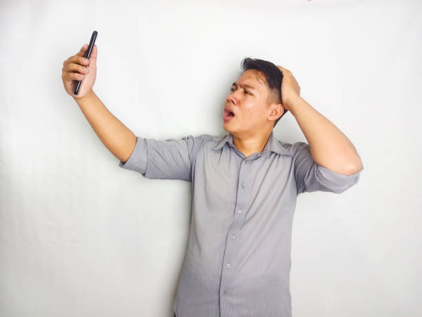 istock A Young man showing disappointed expression when looking to his mobile phone, wearing grey shirt isolated on white background 2175155307