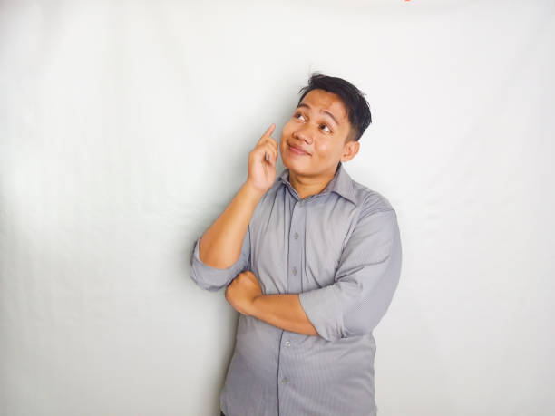 Young Asian man showing thinking pose while his eyes looking to the side wearing grey shirt isolated on white background